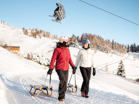 Il Lahnerhof: un hotel al Monte Cavallo, Vipiteno Due donne con slittini su pendio innevato sotto seggiovia
