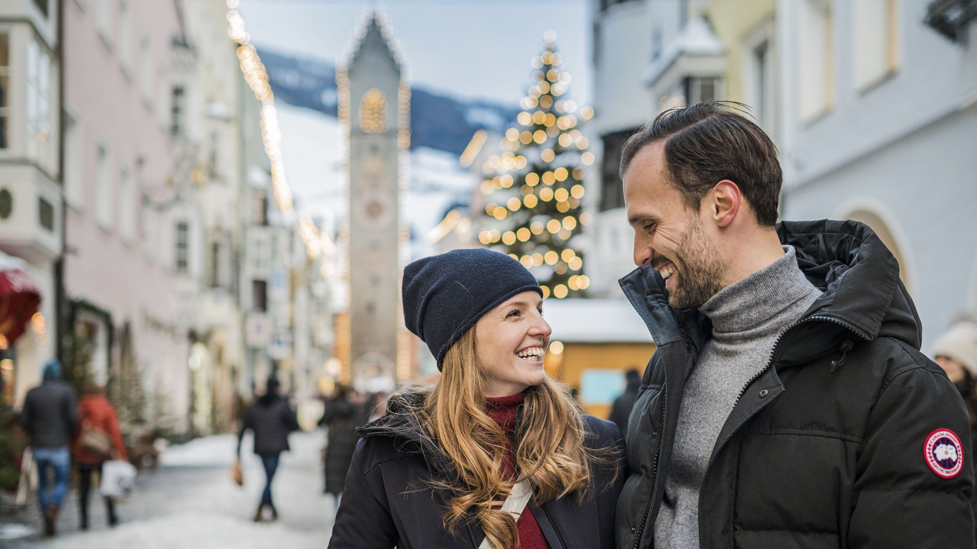 Escursioni sul Monte Cavallo e tanto altro Coppia che sorride in centro storico invernale con albero di Natale e torre sullo sfondo