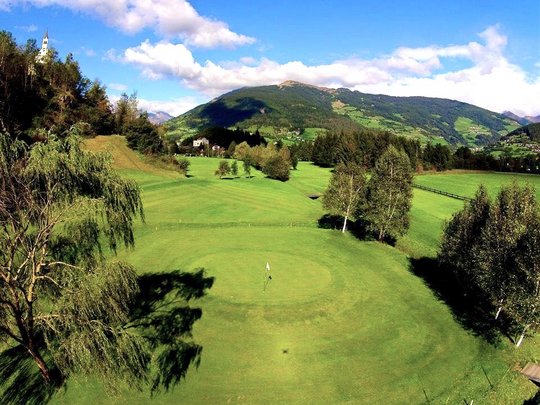 Wandern in Ratschings und Umgebung Golfplatz vor grünen Bergen und Kirche im klaren Himmel