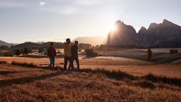 Vi piacciono le escursioni con le ciaspole a Vipiteno? Tre escursionisti camminano al tramonto in un paesaggio montano con baite