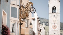 Vi piacciono le escursioni con le ciaspole a Vipiteno? Insegna storica su case colorate con torre campanaria sullo sfondo