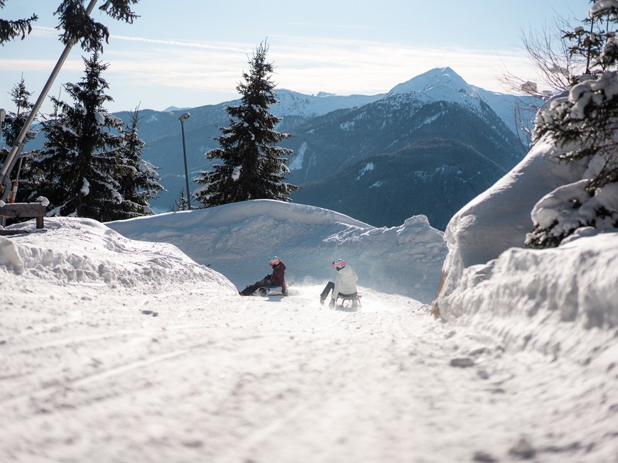 Il Lahnerhof: il vostro hotel vicino a Vipiteno centro Due persone slittano su un sentiero innevato con alberi e montagne sullo sfondo