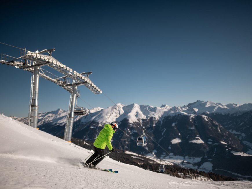 Il Lahnerhof: un hotel al Monte Cavallo, Vipiteno Sciatore con giacca verde scende sulla neve vicino a impianto di risalita e montagne