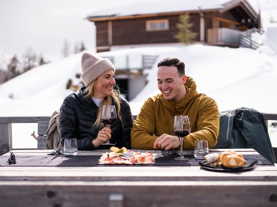Il Lahnerhof: un hotel al Monte Cavallo, Vipiteno Coppia che gusta vino e cibo all'aperto nella neve davanti a una baita