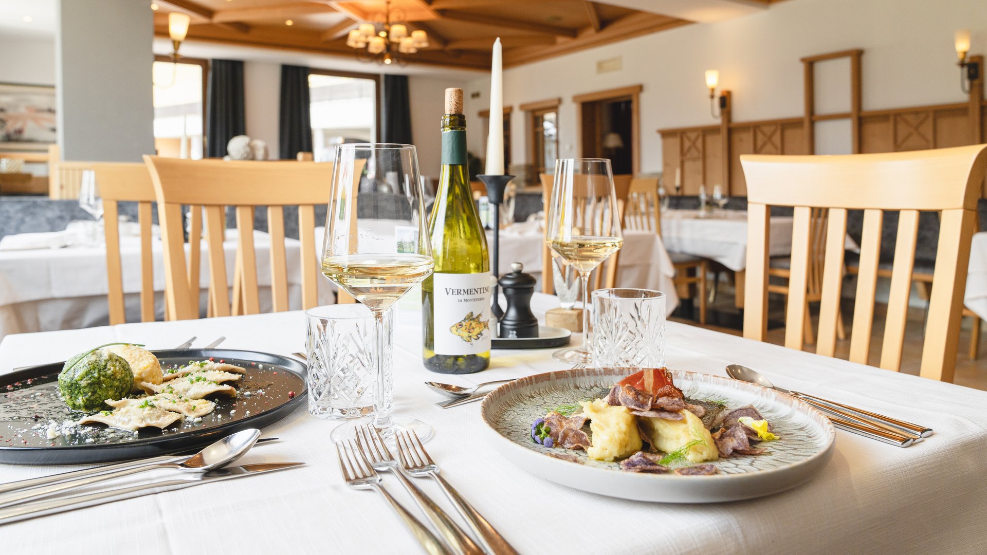 Il Lahnerhof: il vostro hotel vicino a Vipiteno centro Ristorante elegante con due piatti gourmet e vino bianco su tavolo apparecchiato