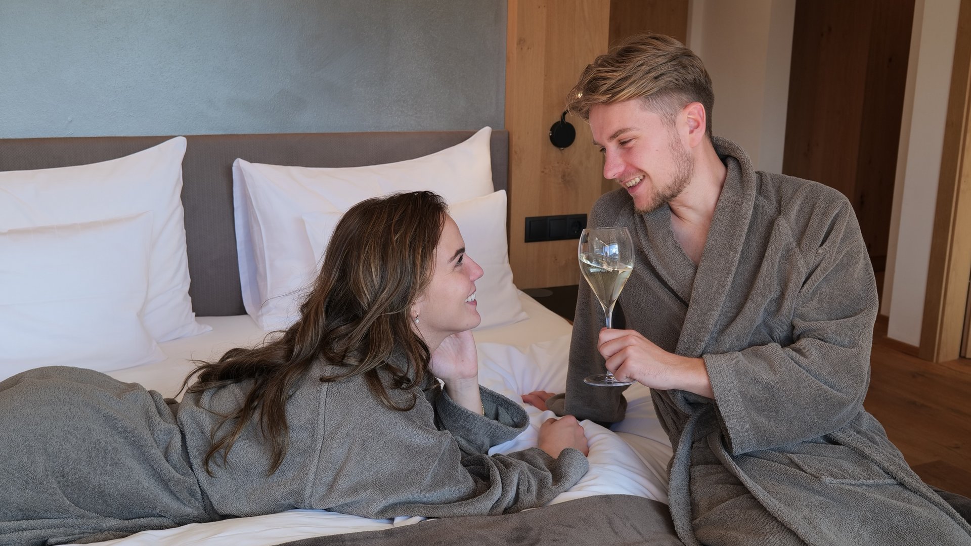 Lahnerhof: Natur- und Wellnesshotel bei Sterzing Paar in Bademänteln entspannt sich auf Bett mit Wein in gemütlichem Schlafzimmer