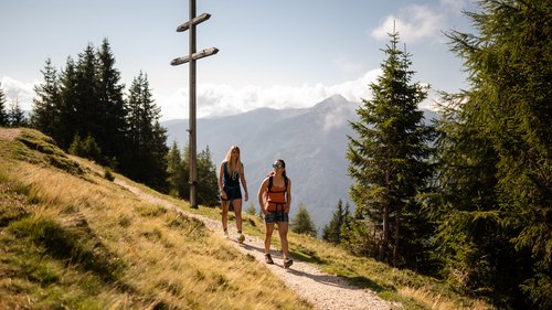 Il Lahnerhof: il vostro hotel vicino a Vipiteno centro Due escursioniste su sentiero di montagna vicino a grande croce di legno