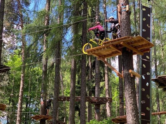 Wandern in Ratschings und Umgebung Kind fährt im Hochseilgarten mit Sicherheitsgurt Fahrrad auf Plattform