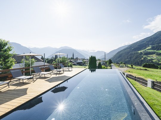 Cercate un hotel a Vipiteno con spa? Benvenuti al Lahnerhof! Piscina a sfioro con lettini e vista sulle montagne sotto un cielo limpido