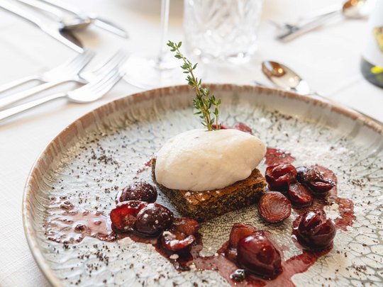 Benvenuti nel ristorante del nostro hotel con spa a Vipiteno Dessert con panna montata, ciliegie e ramo di erbe su piatto