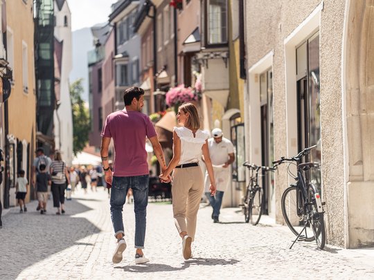 Wandern in Ratschings und Umgebung Paar geht hand in hand durch eine belebte Stadtstraße bei Sonnenschein